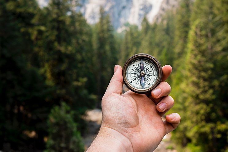 Mountain hiker navigating his way in forest holding a compass