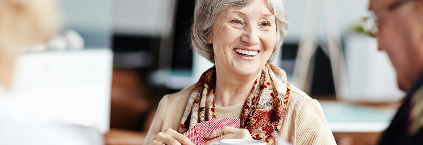 Older lady enjoying catching up with friends over a coffee and a game of cards