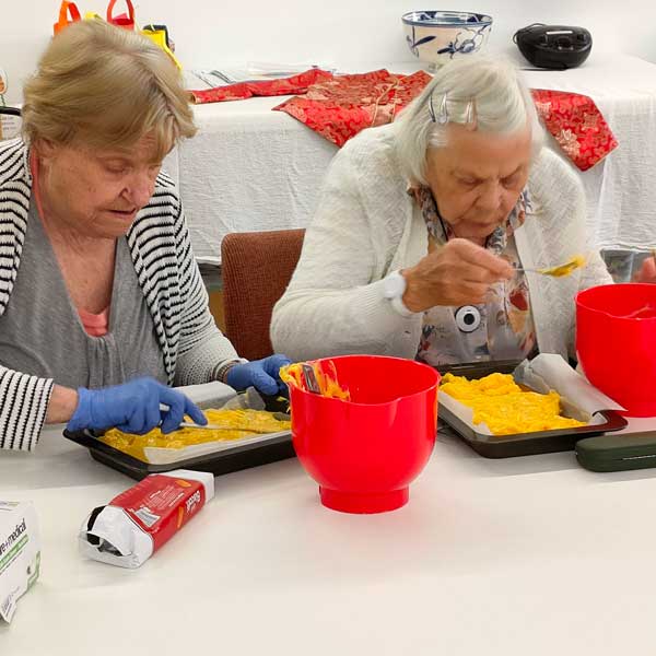 Two older women layering no bake passionfruit custard slice