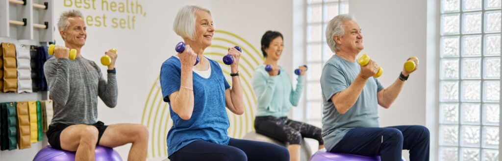 Group of older people in a gym, exercising with weights to improve their balance for April Falls month.