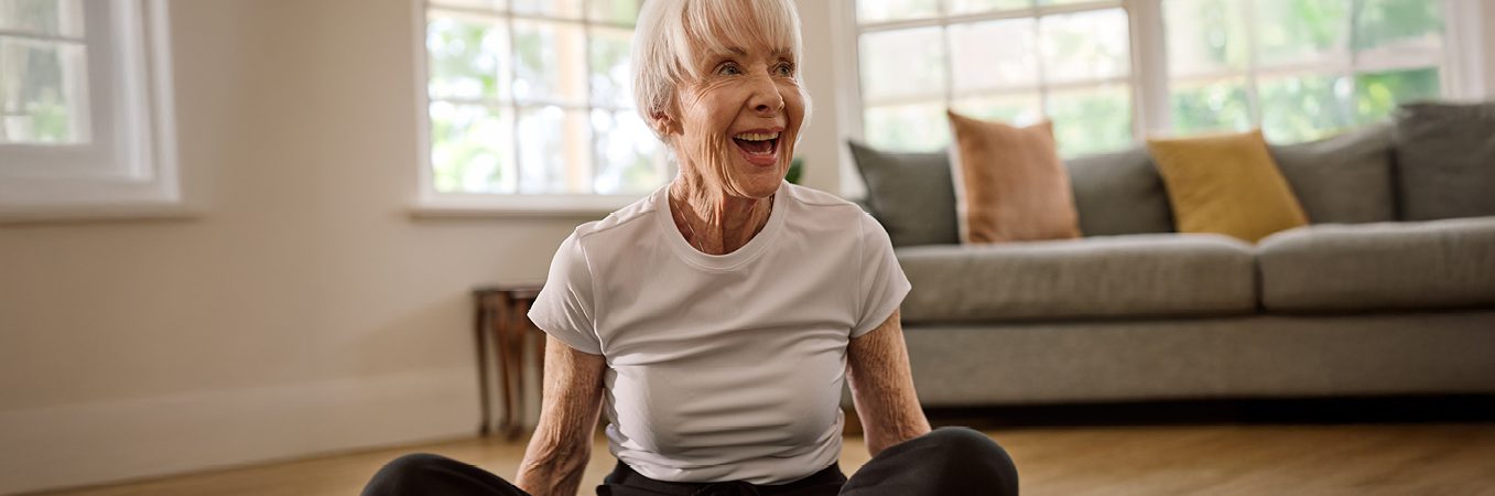 A happy customer, sitting at home with legs crossed, smiling, because she switched to ACH Group's Support at Home services