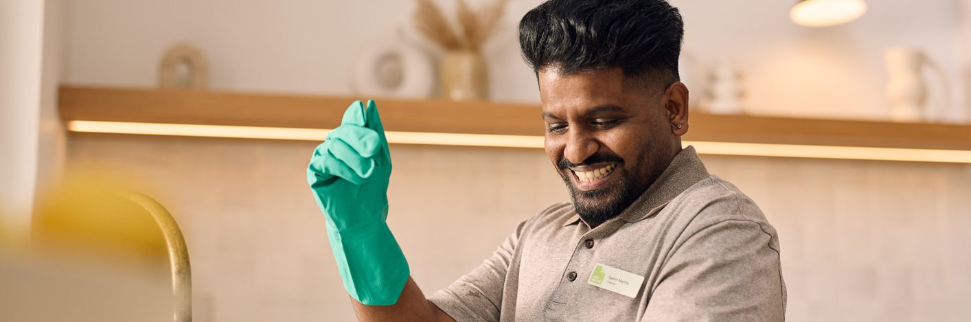 ACH Group cleaner washing dishes, wearing cleaning gloves. Smiling, happy, engaged